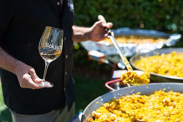 An employee holds a glass of white wine while serving paella