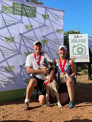 A couple of runners with medals hold a dog next to a selfie picture station