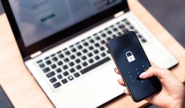 Hand holding locked phone in front of laptop computer