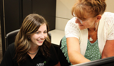 Trainer and intern smiling in front of a computer